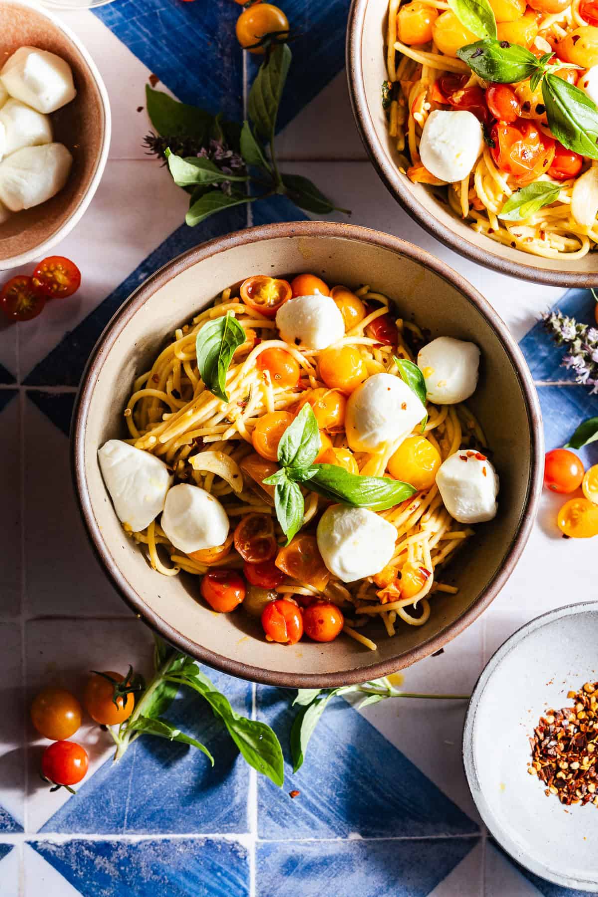 Bowls of blistered cherry tomato pasta with mozzarella and basil.