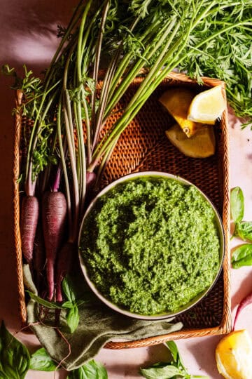 A bowl with carrot top pesto in a basket with the ingredients.