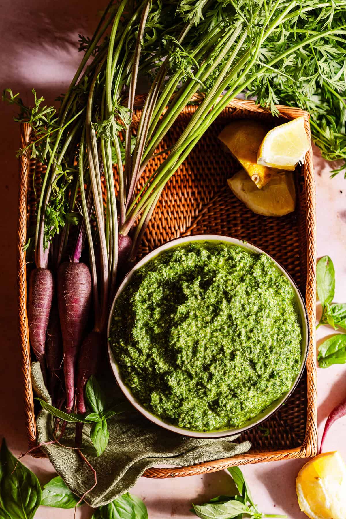 A bowl with carrot top pesto in a basket with the ingredients.