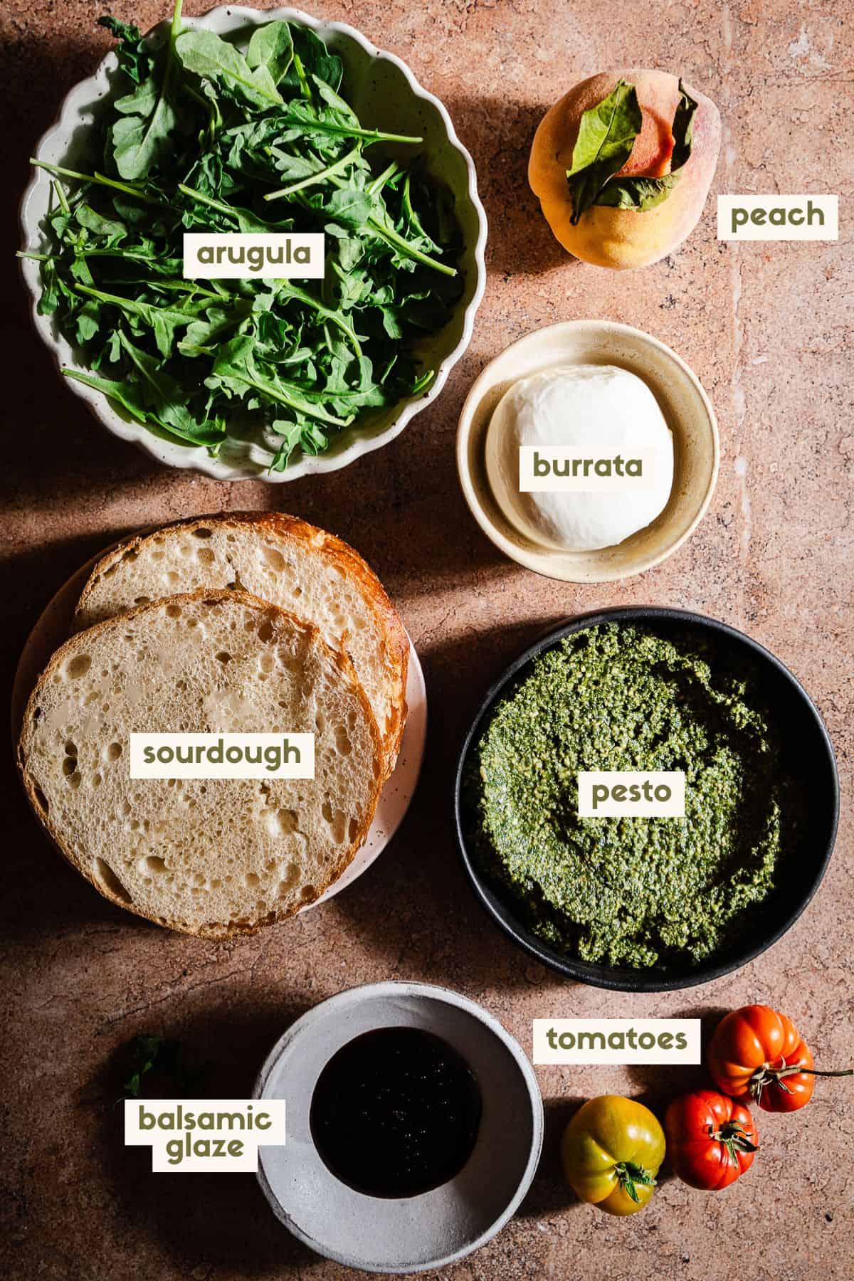 Arugula, peach, burrata, sourdough, pesto, balsamic glaze, tomatoes ingredients with labels.