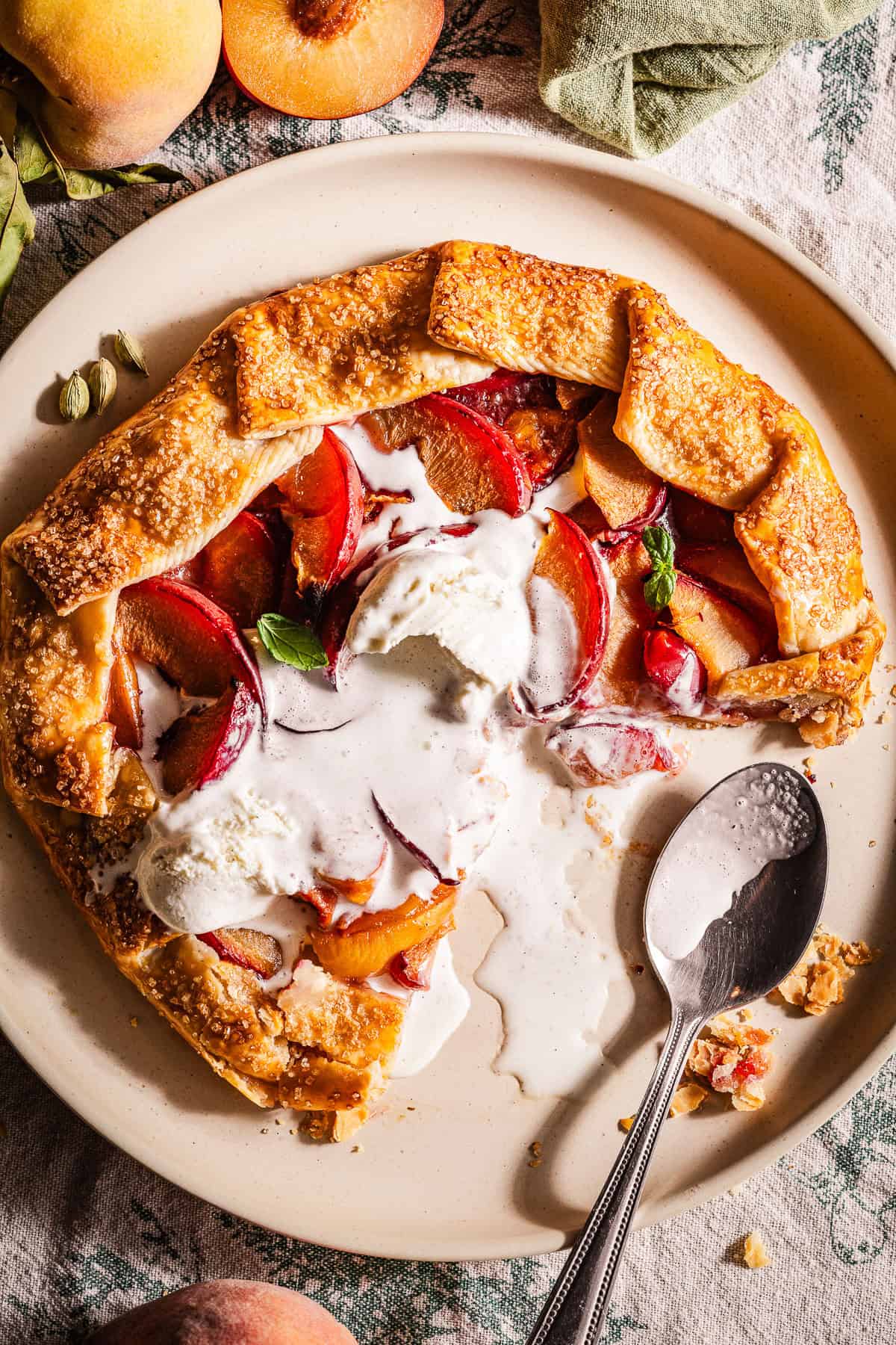 A galette in a plate with peaches and plums and topped with melted ice cream.