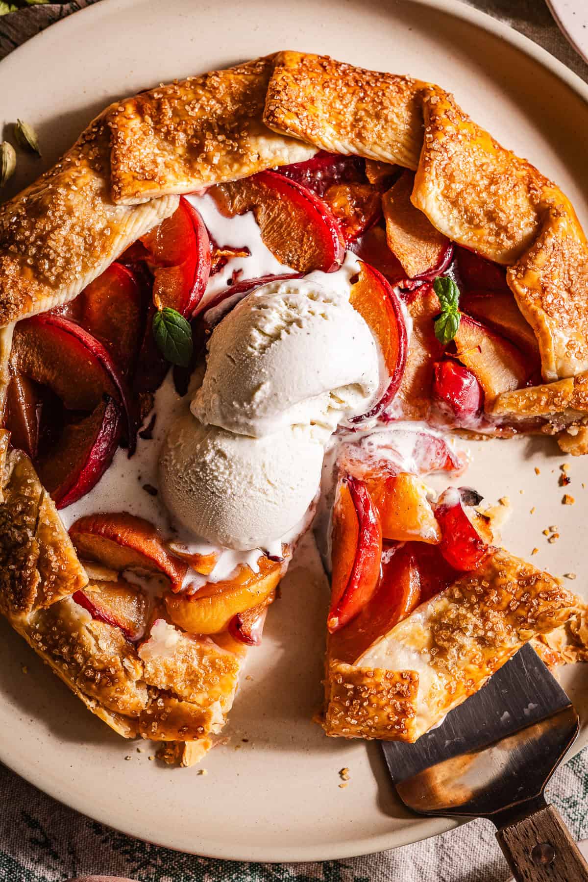 A galette in a plate with peaches and plums and topped with ice cream.