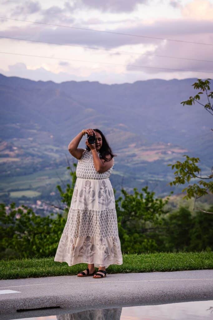 Shweta taking a photo with her camera in a white dress by a pool in Florence.