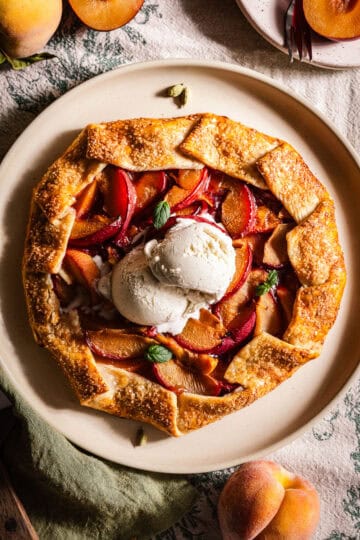 A galette in a plate with peaches and plums and topped with ice cream.