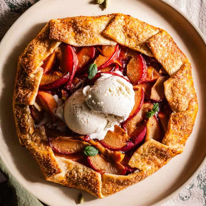 A galette in a plate with peaches and plums and topped with ice cream.