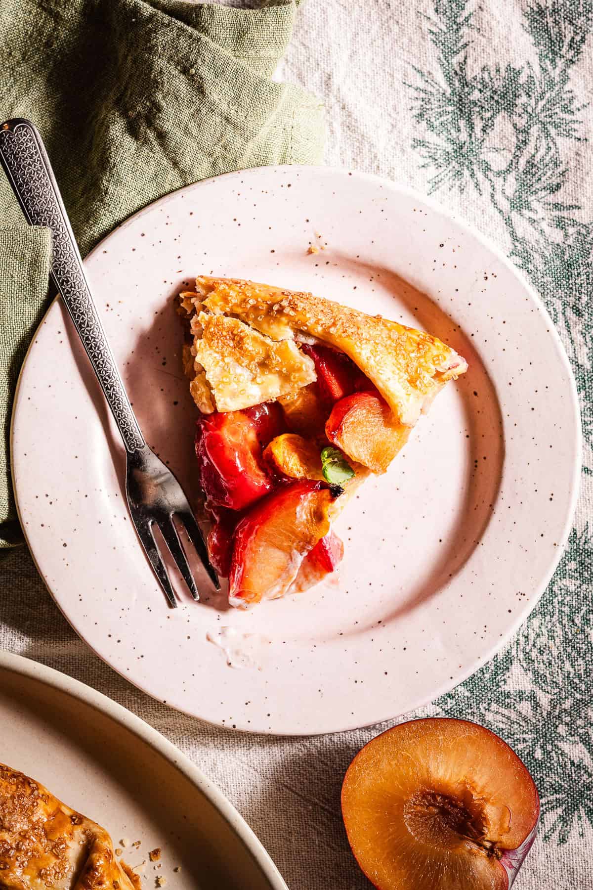 A slice of stone fruit galette galette in a dessert plate with a dessert fork.