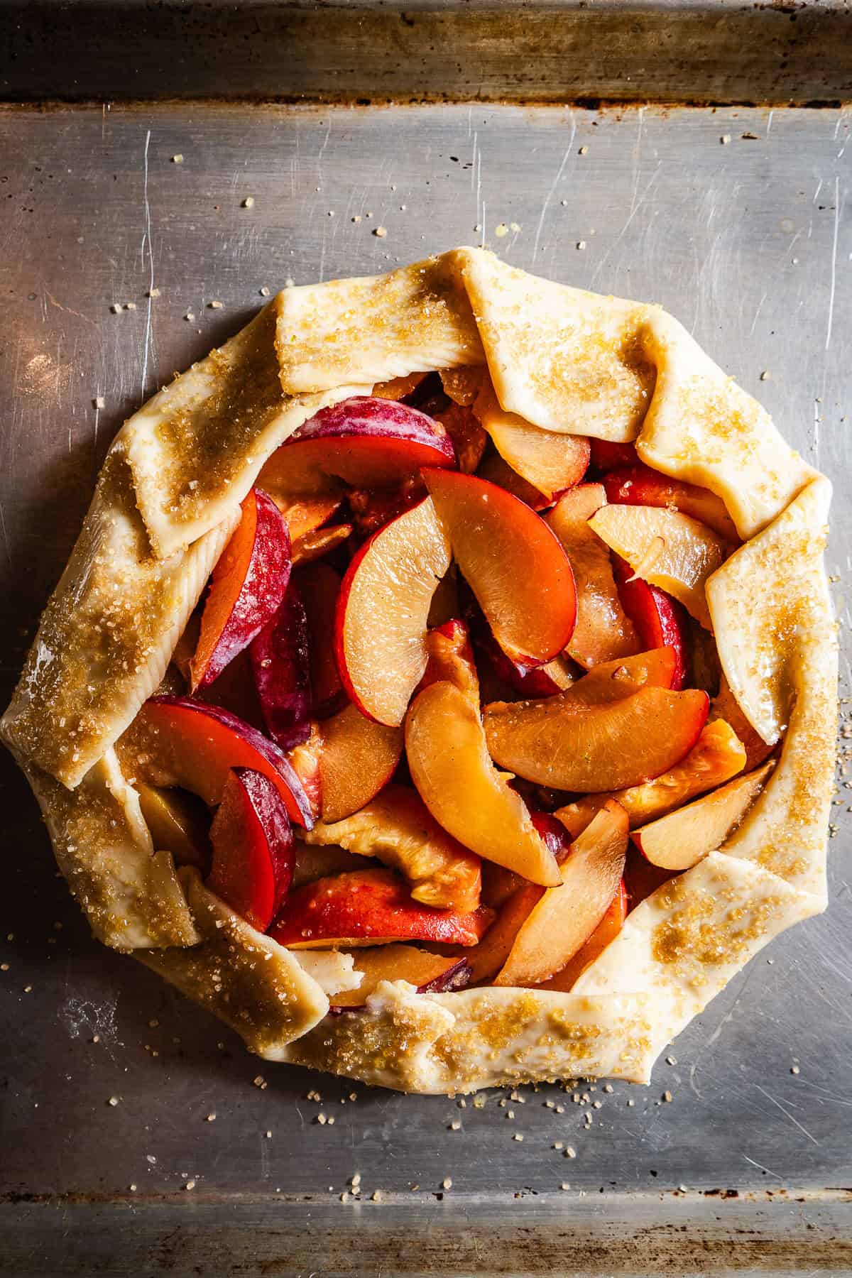 An unbaked galette with plums and peaches on top.