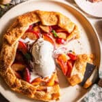 A galette in a plate with peaches and plums and topped with ice cream.