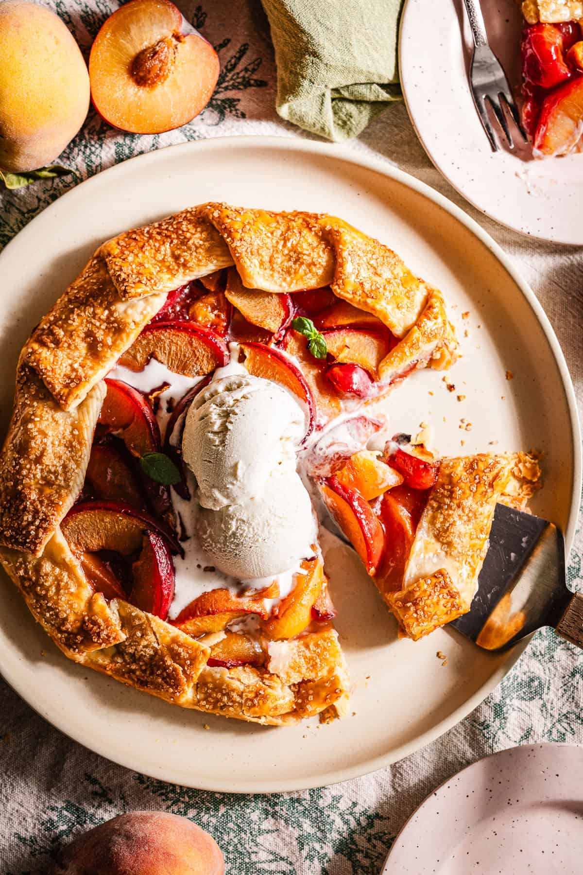 A galette in a plate with peaches and plums and topped with ice cream.