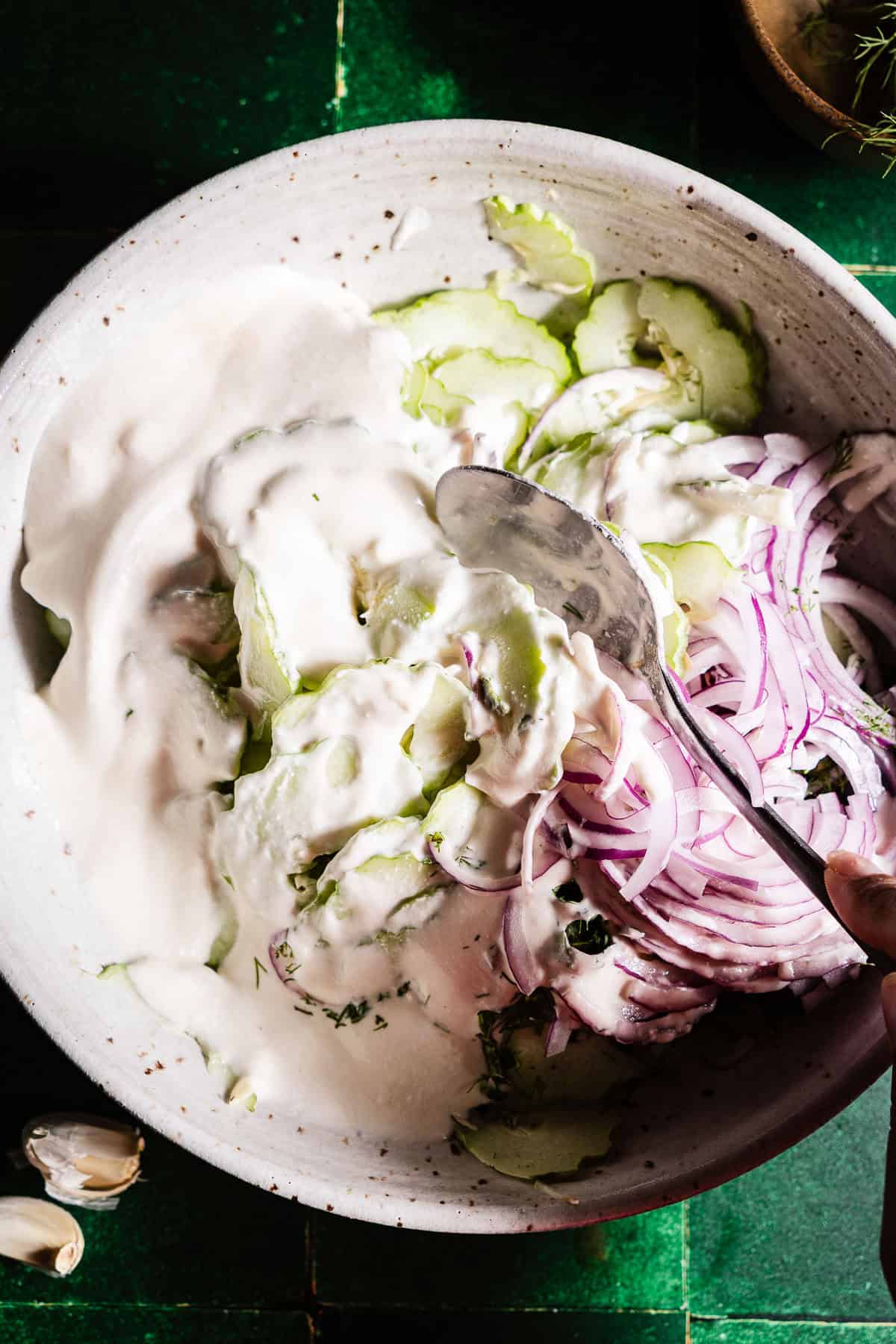 Mixing in a yogurt sauce into a creamy cucumber salad.