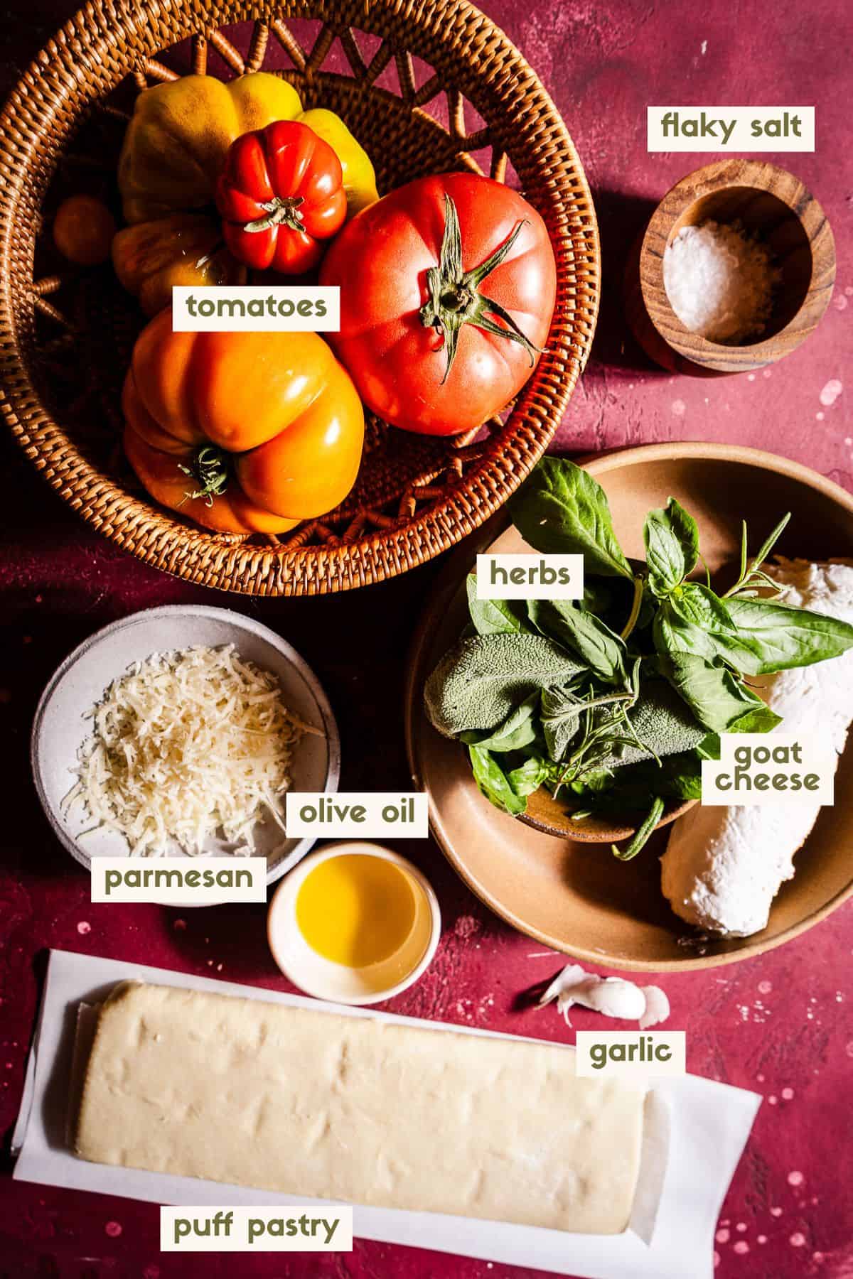 Tomatoes, flaky salt, herbs, goat cheese, olive oil, parmesan, garlic, and puff pastry ingredients with labels.